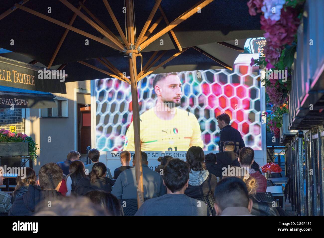 Menschen, die das Fußballspiel der Euro 2020 auf einem Pub-Sitzplatz im Freien beobachten, der italienische Torwart Gianluigi Donnarumma auf dem Bildschirm Stockfoto