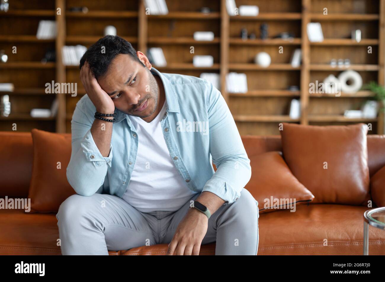 Frustrierter indischer Mann fühlt Zweifel und Verzweiflung, sitzt mit verärgerter Gesichtsausdruck auf dem Sofa und hält den Kopf, östlicher Kerl fühlt Kopfschmerzen und Depressionen, leidet an Reue Stockfoto