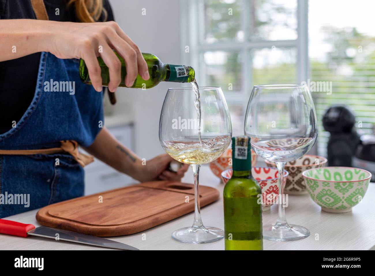 Frau in der Küche gießt zwei Gläser Weißwein, während sie kocht Stockfoto