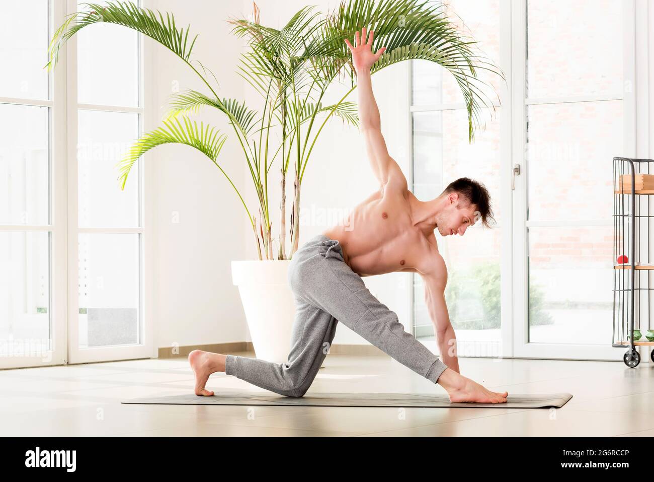Junger Mann, der eine Parivrtta trikonosana oder ein drehtes Dreieck Yoga Pose in einem High-Key-Fitnessstudio mit Copyspace in einem gesunden aktiven Lebensstil Konzept Stockfoto