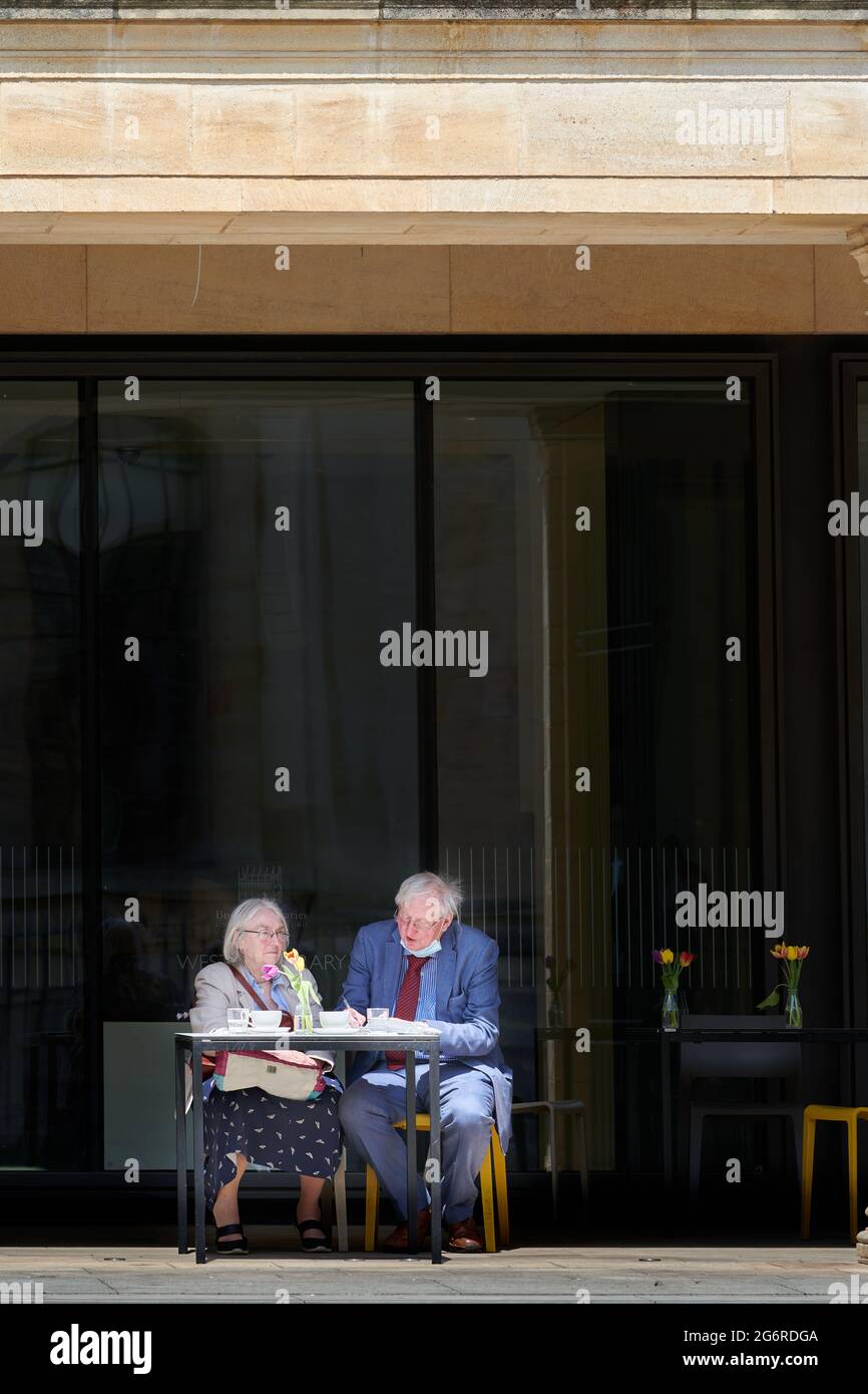 An einem sonnigen Sommertag essen ältere Paare vor dem Café in der Weston-Bibliothek der Universität Oxford, England, zu Mittag. Stockfoto