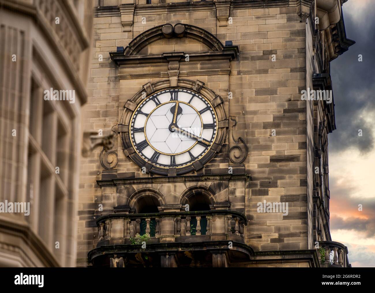 Alter alter Uhrenturm mit Sonnenuntergang hinter goldorangefarbenen Wolken am Himmel. Zwanzig nach zwölf 12:20-Uhr-Zifferblatt mit römischen Ziffern und Zeitanzeige Stockfoto