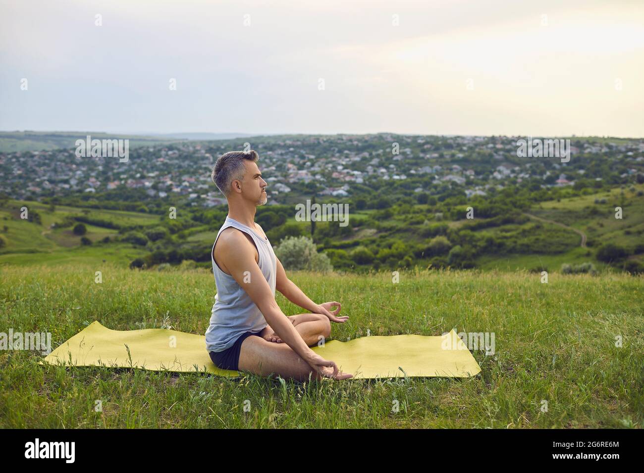 Yoga. Ein Mann mit grauen Haaren praktiziert im Sommer Meditation über die Natur. Stockfoto