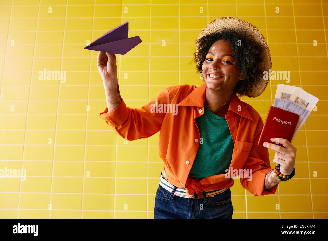 Flugreisekonzept. Lächelnde, multiethnische Frau mit Flugtickets und internationalem Pass wirft ein Papierflugzeug, das Flugreisen simuliert, über Gelb Stockfoto