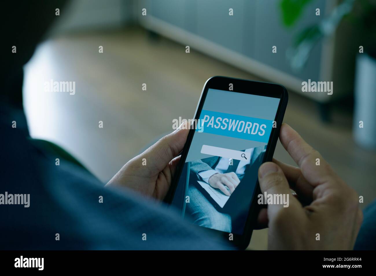 Ein junger Mann, der zu Hause sitzt, verwendet einen Passwort-Manager in seinem Smartphone, mit einer verspotteten Passwort-Manager-App auf dem Bildschirm Stockfoto