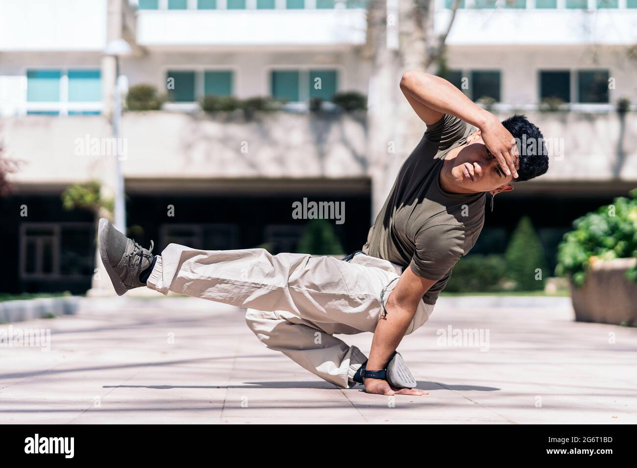 Hispanischer junger Mann, der im Park Breakdance-Bewegungen macht und die Kamera anschaut. Stockfoto
