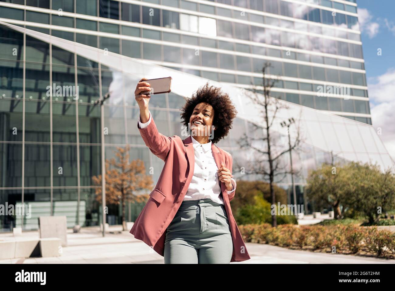 Glückliche schwarze Geschäftsfrau mit afro Haaren lächelnd und Selfie mit ihrem Handy. Stockfoto