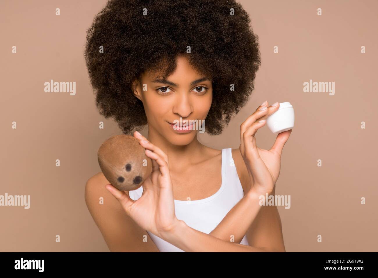 Eine junge, hübsche, lockige Mulatta mit einer Kokosnuss und einem Glas Creme Stockfoto