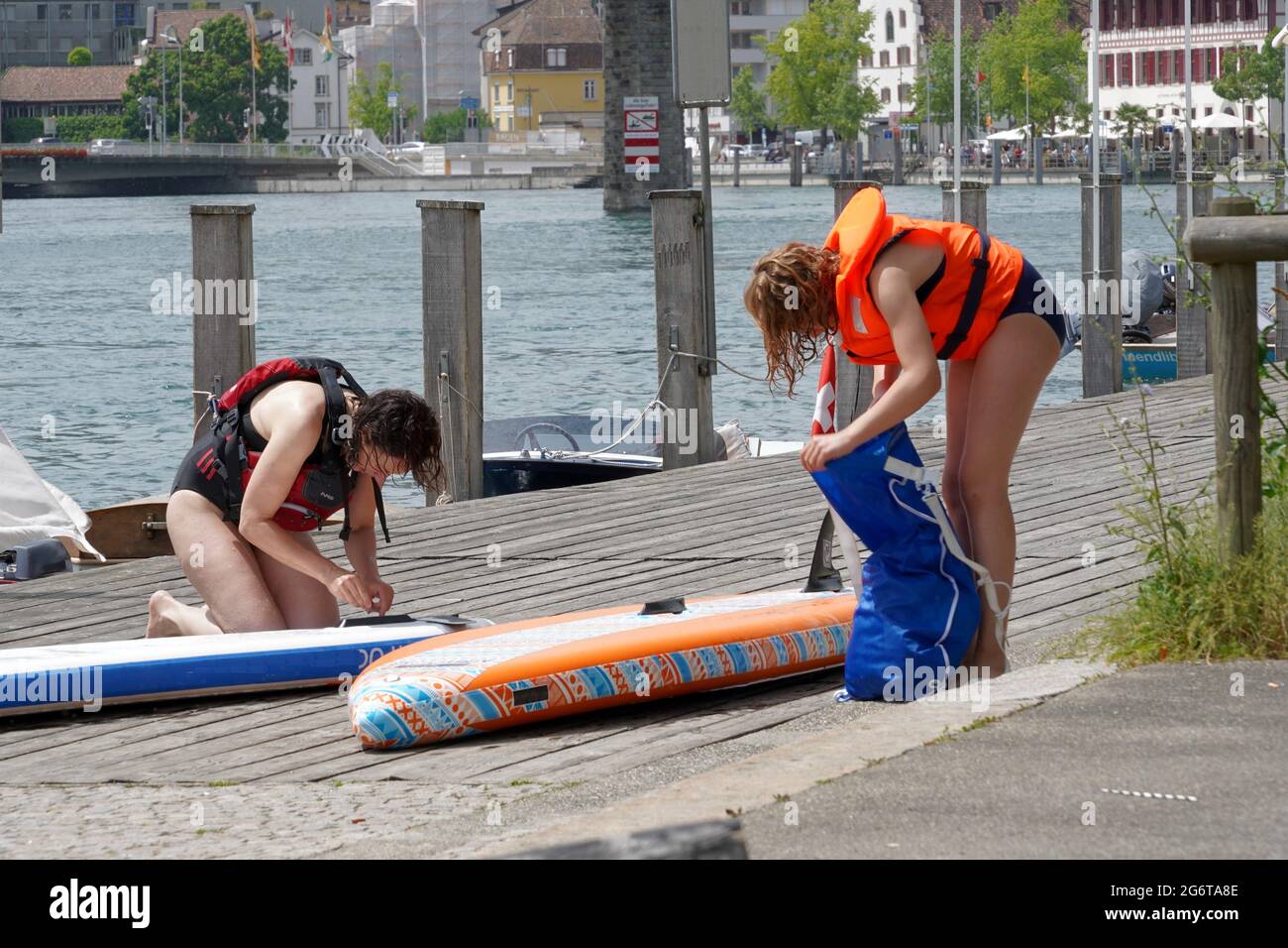 Zwei Frauen in Schwimmwesten packen ihre Stand Up Paddle Boards nach einer Fahrt auf dem Rhein in Schaffhausen Schweiz. Sie befinden sich am Flusspier. Stockfoto