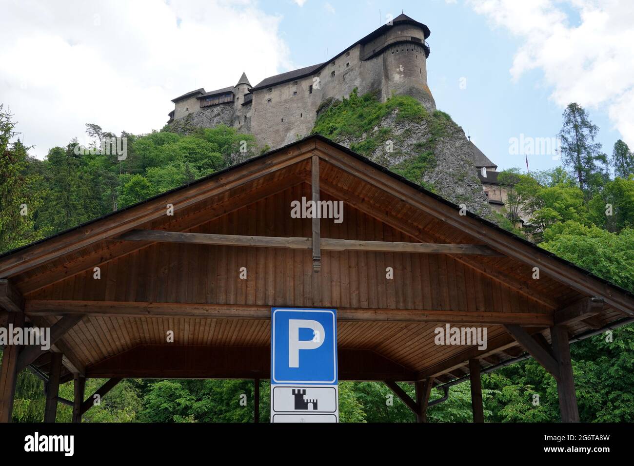 Parkplatz aus Holz mit Verkehrsschild zum Parken im Bereich um die Orava Burg in der Slowakei. Low-Angle-Ansicht mit der Silhouette einer Burg. Stockfoto