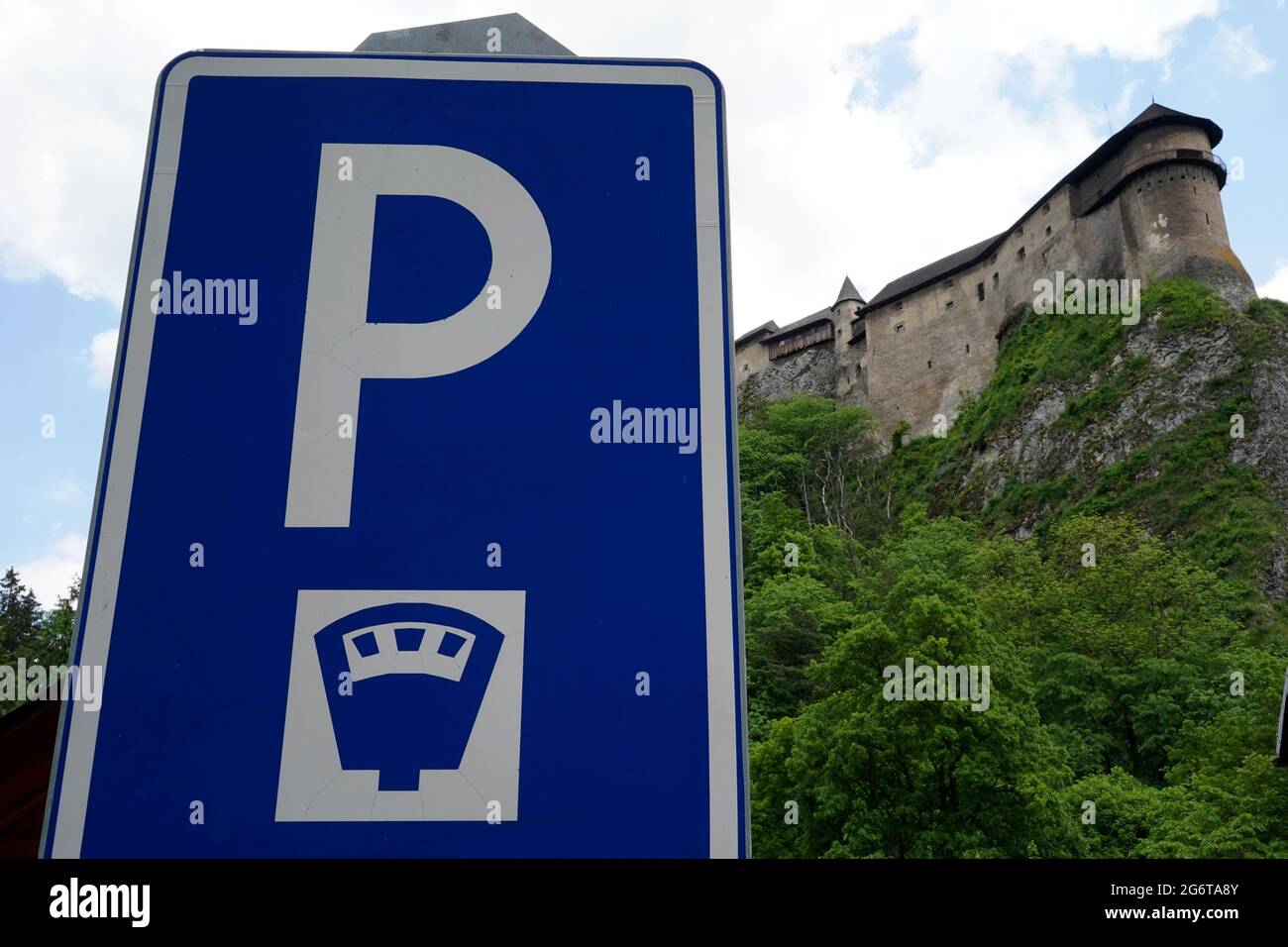 Verkehrsschild für kostenpflichtige Parkplätze im touristischen Bereich rund um die Orava Burg in der Slowakei. Low-Angle-Ansicht mit der Silhouette der Burg im Hintergrund. Stockfoto