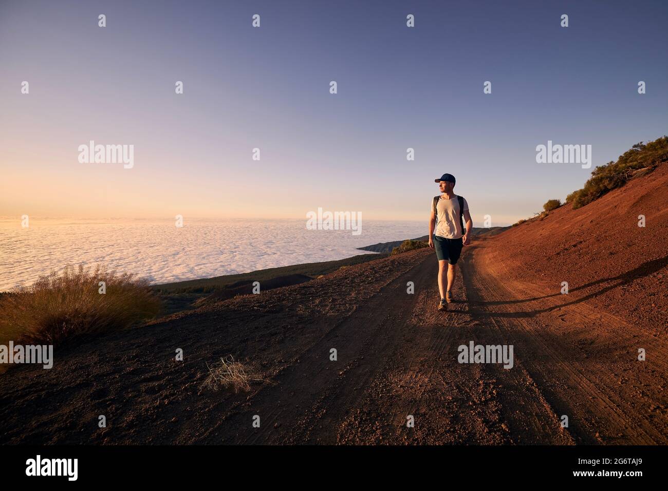Mann genießen Blick über Wolken. Junger Wanderer, der bei Sonnenuntergang auf unbefestigterem Weg gegen die Landschaft geht.Teneriffa, Kanarische Inseln, Spanien. Stockfoto