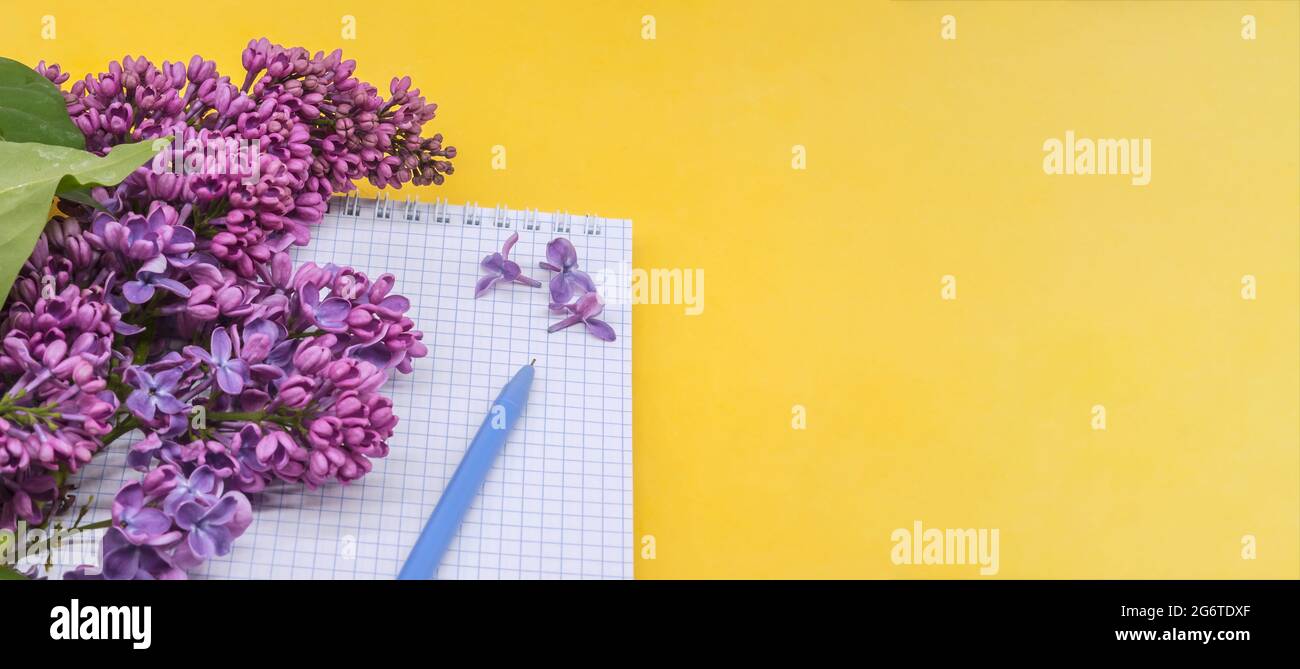 Notizblock mit Stift und Blumen. Spiralnotizbuch und Stift. Notebook-Flieder auf gelbem Hintergrund. Stockfoto