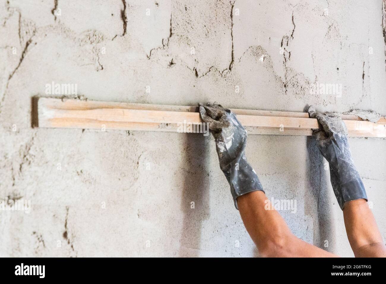 Arbeiter verputzt Zementmörtel auf Betonwand mit langer Holzkelle Stockfoto