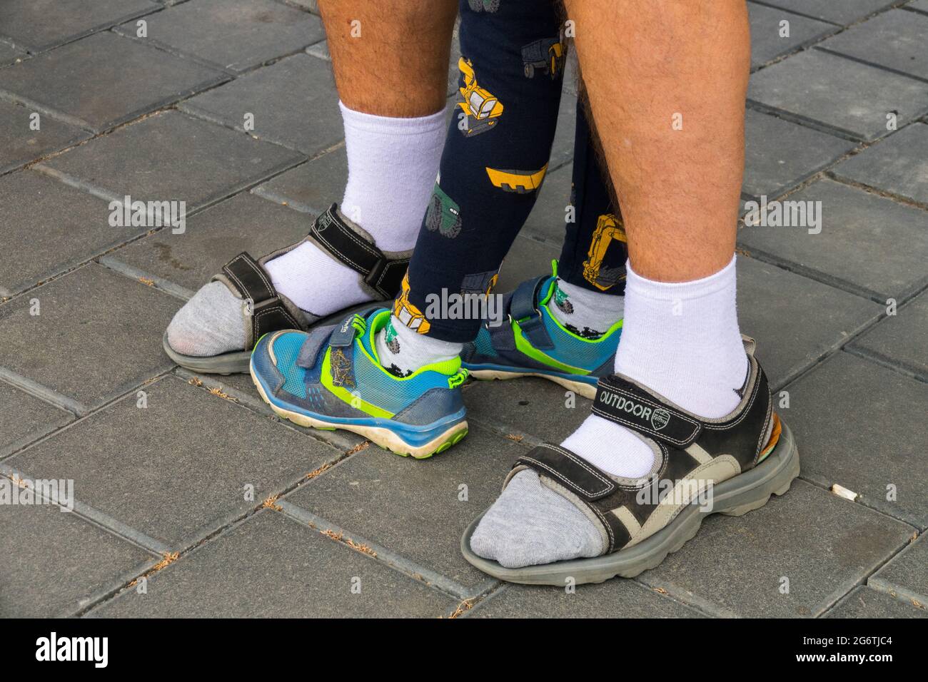Senior-Mann-Socken in Sandalen und Kinder-Turnschuhe alt und jung, Schuhgeneration männliche Füße Stockfoto