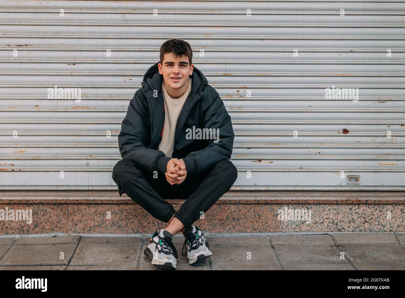 Lässiger junger Mann, der auf der Straße der Stadt sitzt Stockfoto