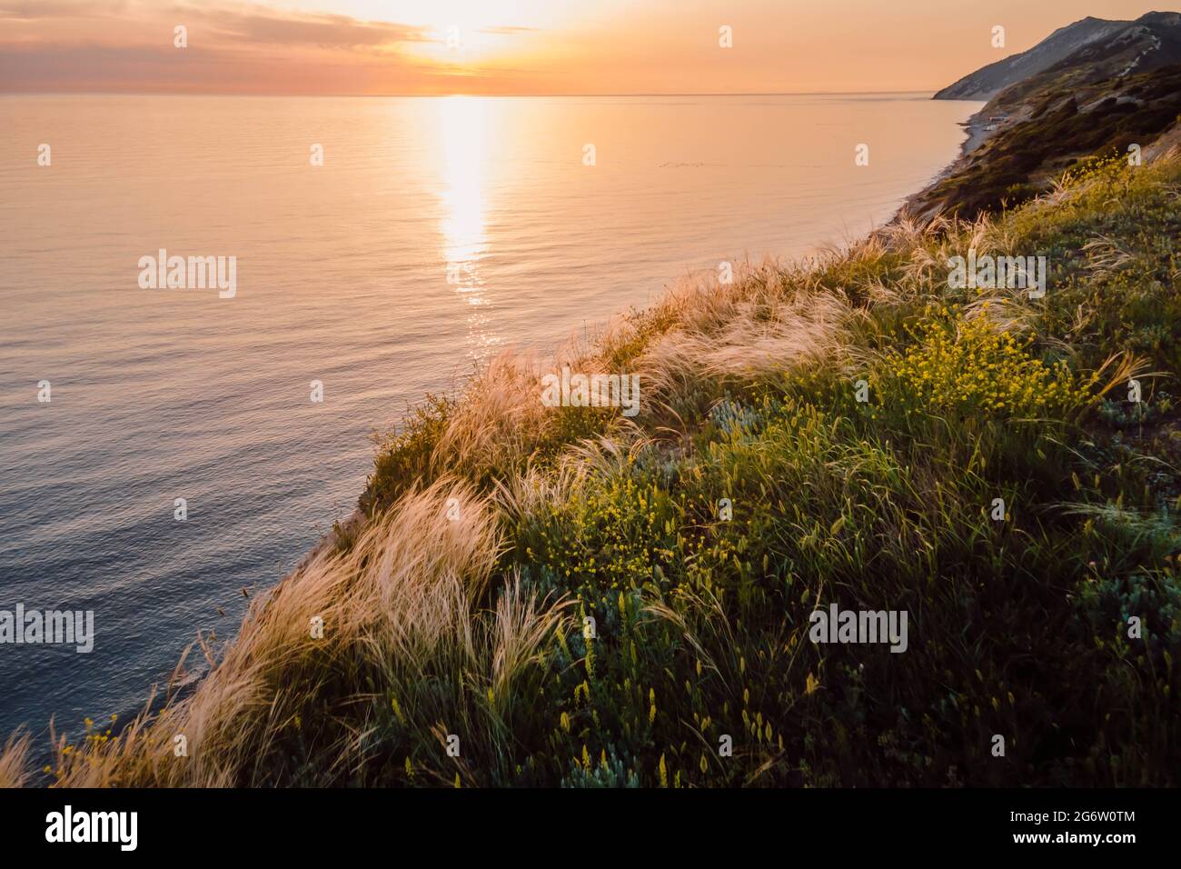Luftaufnahme der Sommerküste mit Gras und ruhigem Meer. Küstenlinie mit Sonnenuntergangsfarben Stockfoto