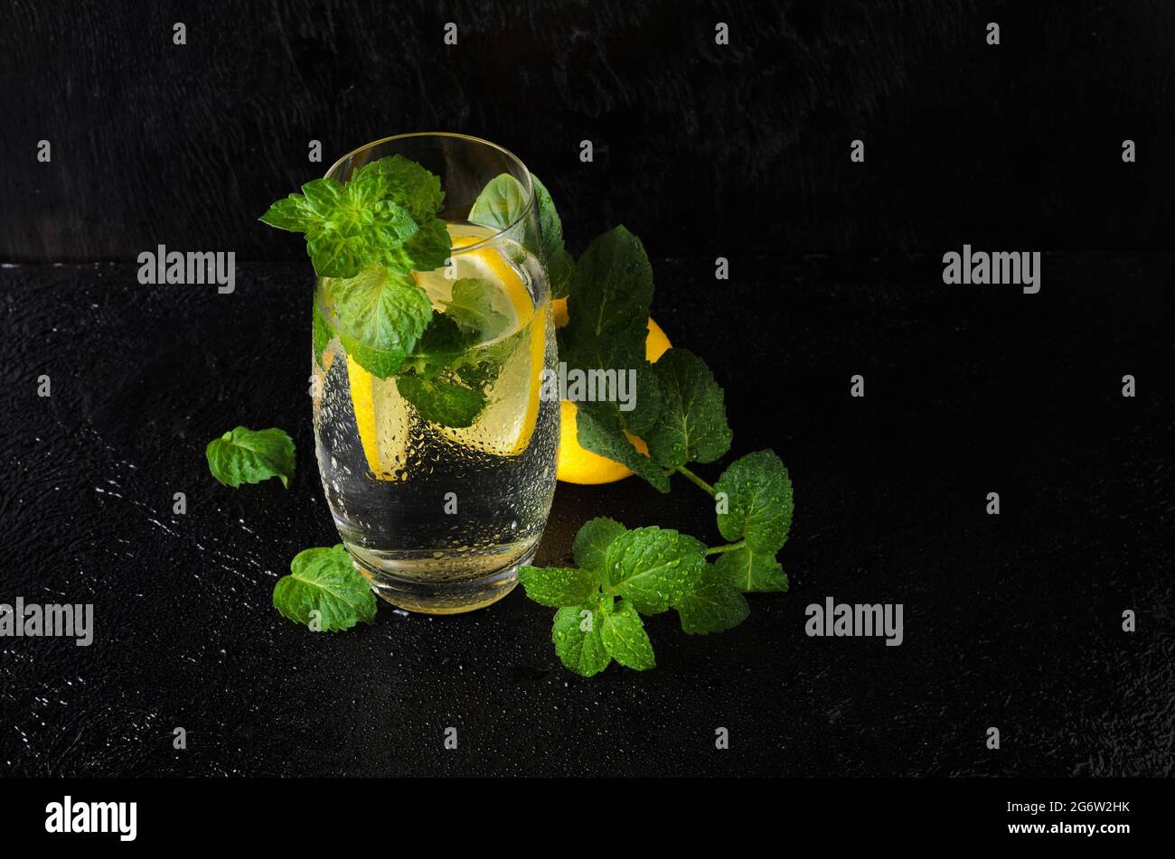 Ein großes Glas Wasser mit Zitrone, Minzblättern und Eis, bedeckt mit Wassertropfen. Ein Glas Limonade auf einem schwarzen strukturierten Hintergrund. Selektiver FOC Stockfoto