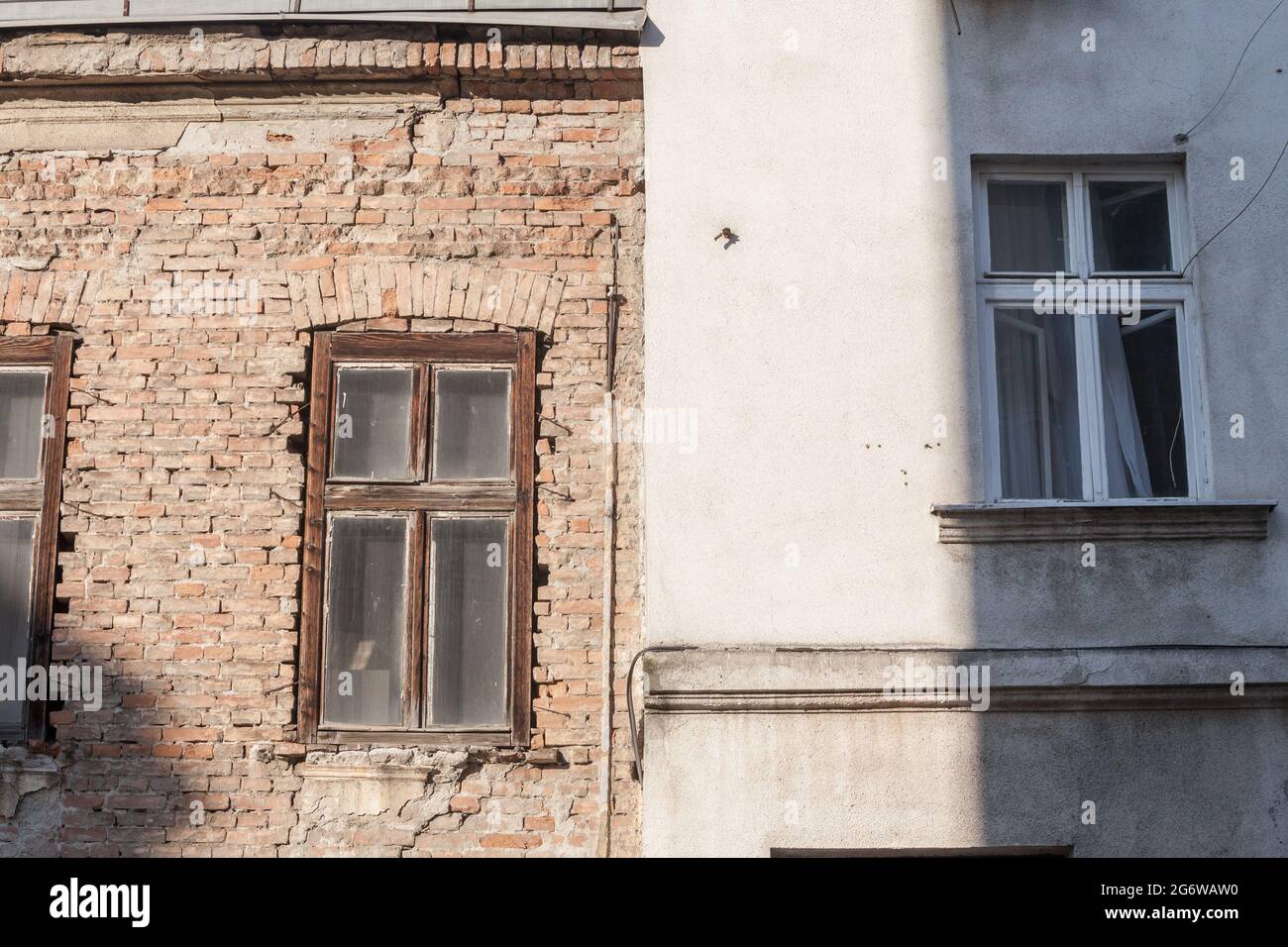 Bild von zwei Fassaden, nebeneinander, eine in rauem und rohem beschädigten roten Ziegel, die andere mit einer weißen Betondichtung. Stockfoto