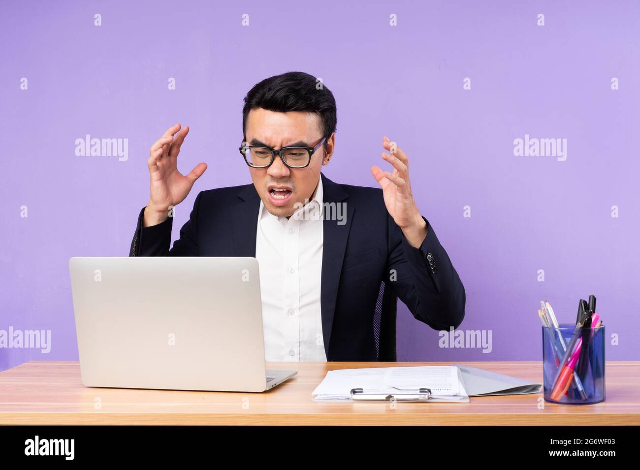Asiatischer Geschäftsmann, männlich, auf Schreibtisch sitzend, isoliert auf violettem Hintergrund Stockfoto