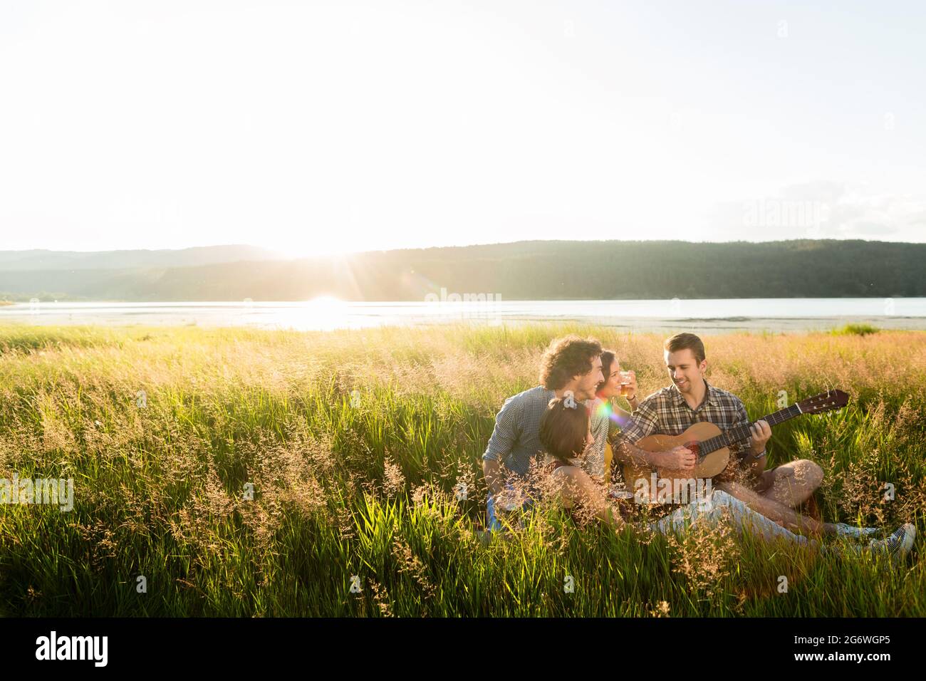 Gruppe von Freunden in Landschaft bei Sonnenuntergang spielen Gitarrenmusik Stockfoto