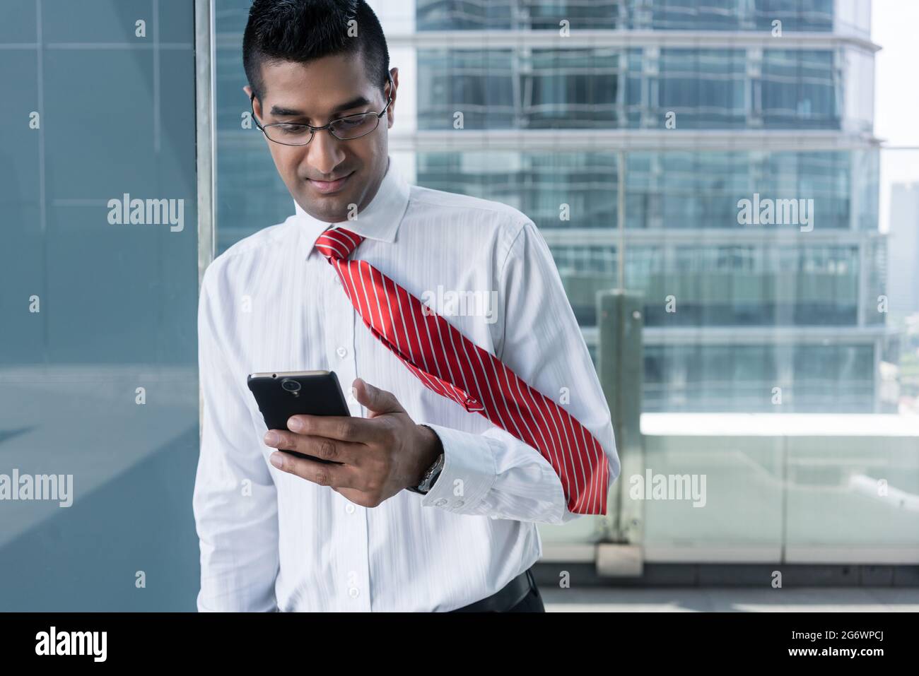 Porträt eines indischen Geschäftsmann Lächeln beim Lesen der Informationen auf dem Mobiltelefon im Innenbereich Stockfoto