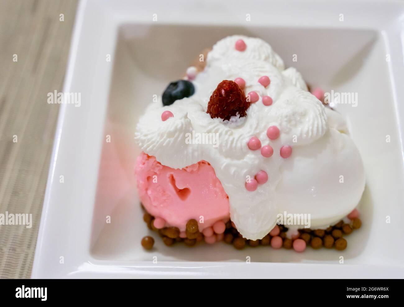 Schräge Ansicht von oben auf Vanille- und Erdbeereis mit Schlagsahne und Beeren, serviert auf einem weißen Dessertgericht, natürliches Licht. Stockfoto