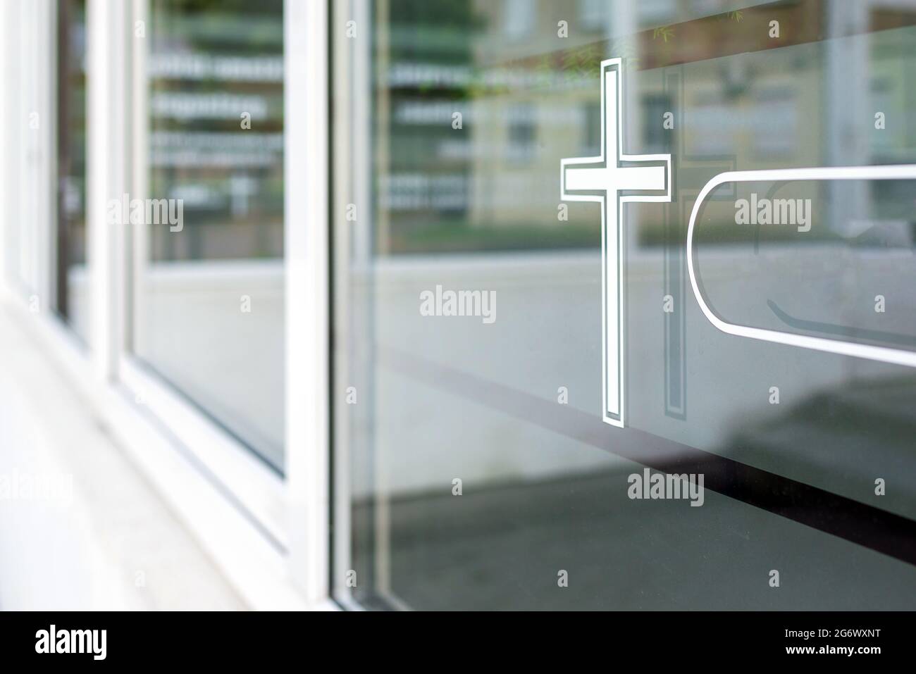 Nahaufnahme eines weißen Kreuzes auf einem Fenster. kirche im Hintergrund.Beerdigungsinstitut Sommertag nach covid-19 Pandemie.leeres Beerdigungsinstitut. Speicherplatz kopieren. Stockfoto