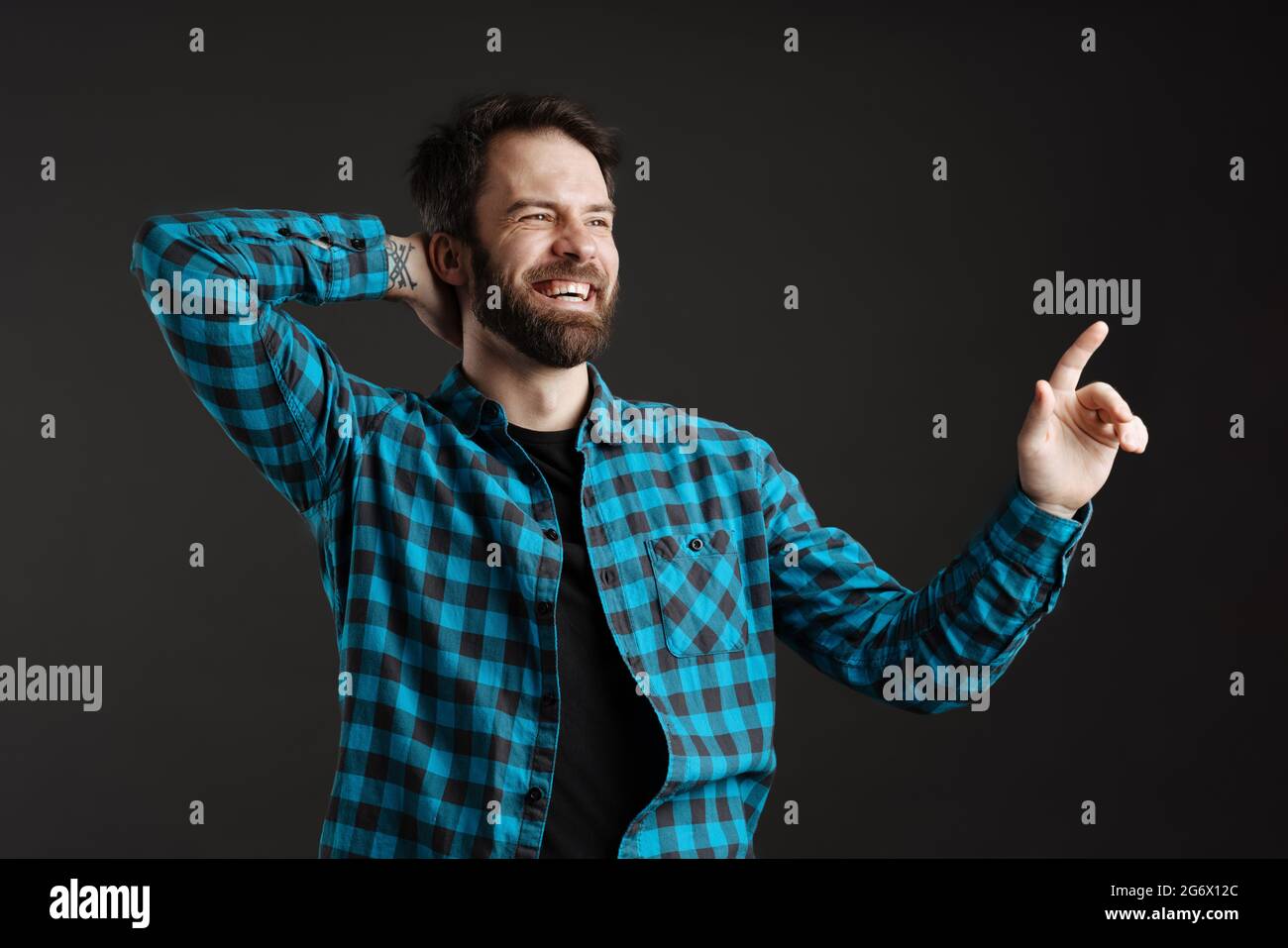 Lächelnder bärtiger Mann, der mit dem Finger nach oben zeigt, während er seinen Hals isoliert auf schwarzem Hintergrund hält Stockfoto
