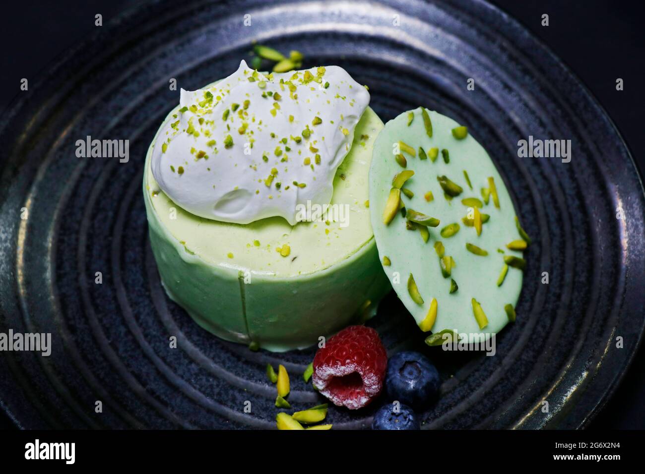 Käsekuchen mit Pistazien-Geschmack, verziert mit Beeren und frischer Creme Stockfoto