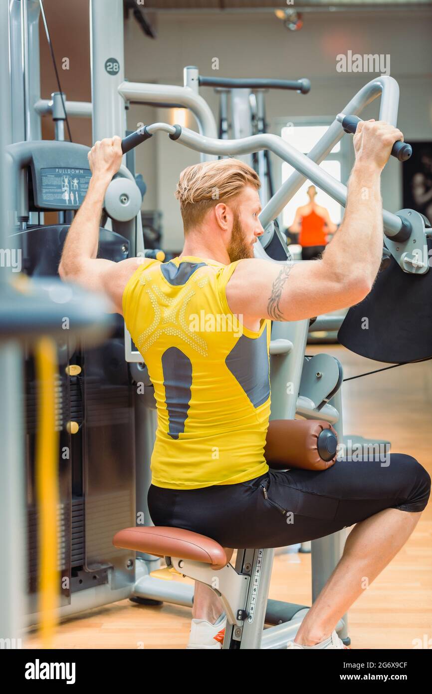 Rückansicht eines leistungsstarken Bodybuilders mit starken Armen, der während des Oberkörper-Workout-Routinetrainings in einem Fitnessclub mit modernen Geräten trainiert Stockfoto