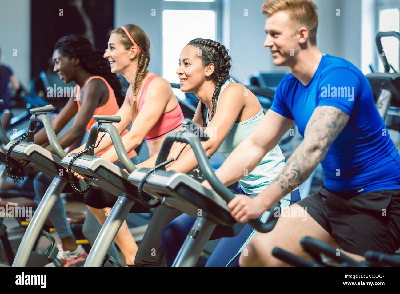 Brunette schöne Frau lächelt, während sie auf einem modernen Fitness-Fahrrad während der Gruppe Spinning-Klasse im Fitnessstudio radelt Stockfoto