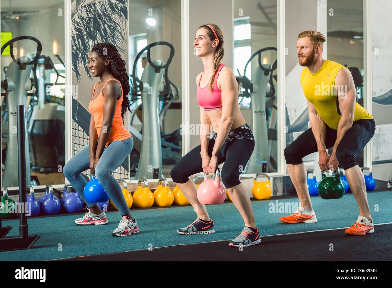 Volle Länge von drei Jungen und Schönen entschlossene Menschen holding Kettlebells während des Trainings Russischen Schaukel bei der funktionellen Ausbildung Klasse am Stockfoto