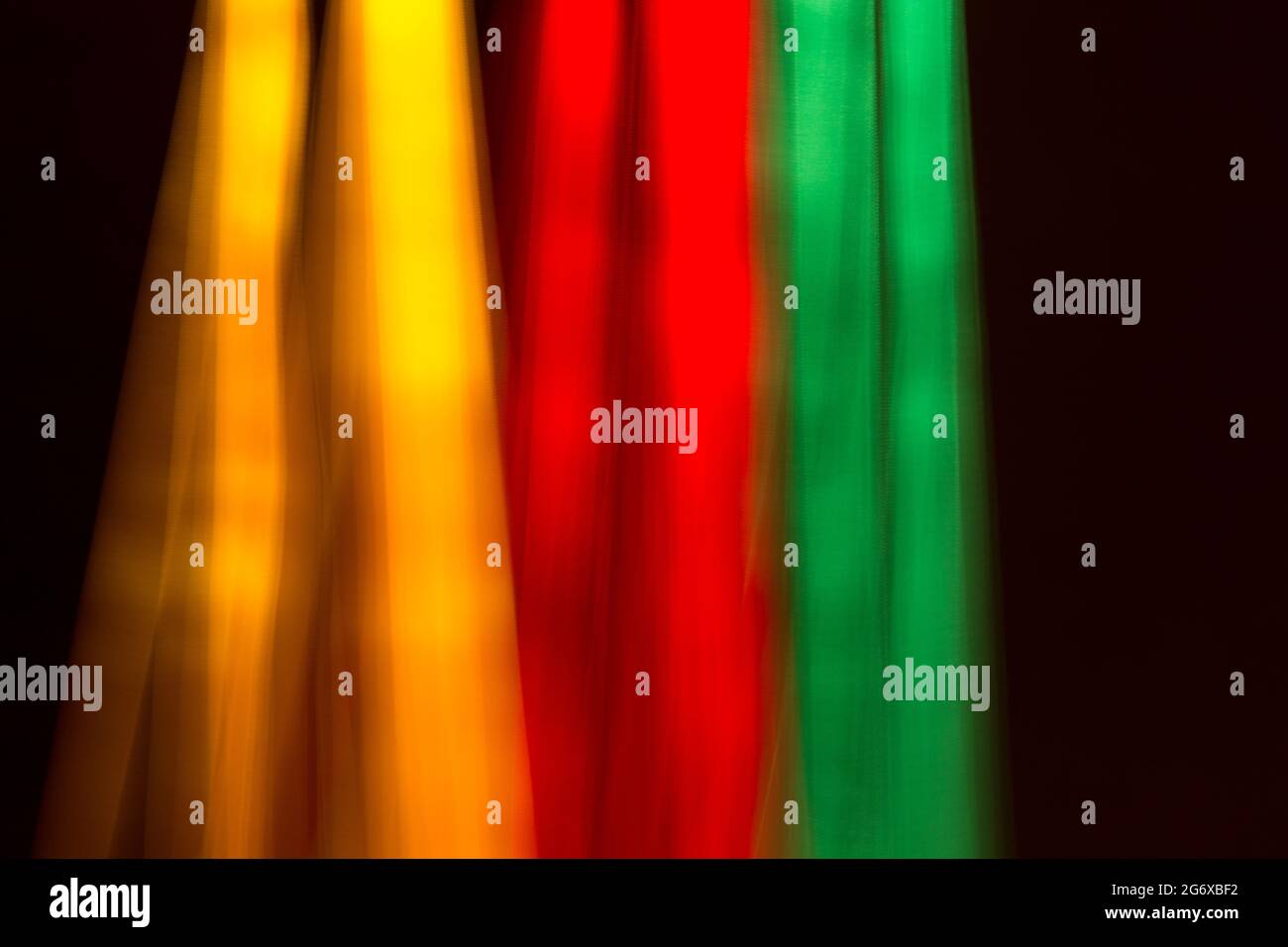 Bewegte Farben von Stoffbändern; verdünnte und verblasste Grundfarben auf schwarzem Hintergrund; Gelb, Rot und Grün, typische Farben von Nationalflaggen. Stockfoto