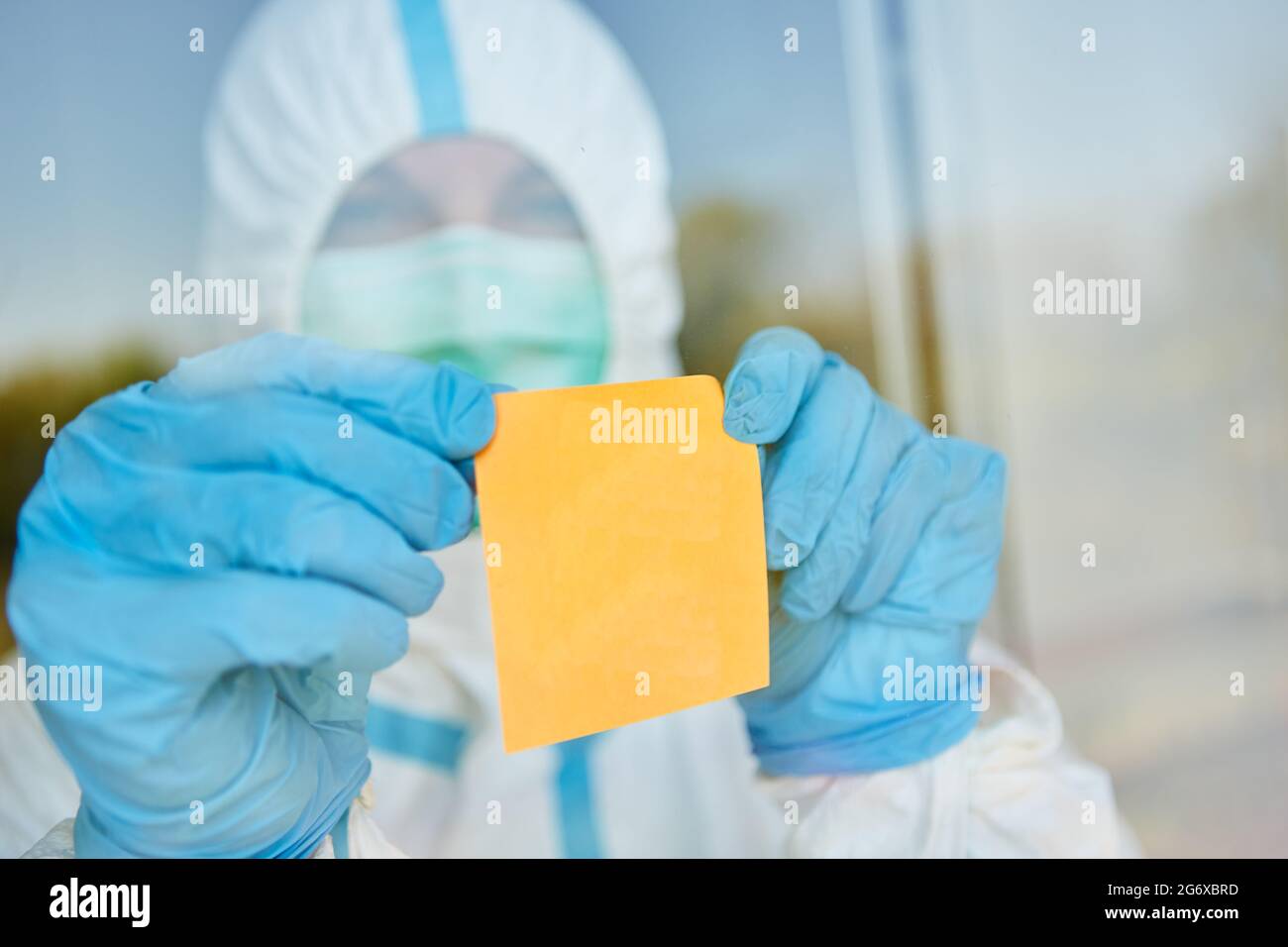 Leere gelbe Haftnotiz ist an der Tür oder dem Fenster der Klinik angebracht, wobei der Arzt während der Coronavirus-Epidemie in Schutzkleidung ist Stockfoto