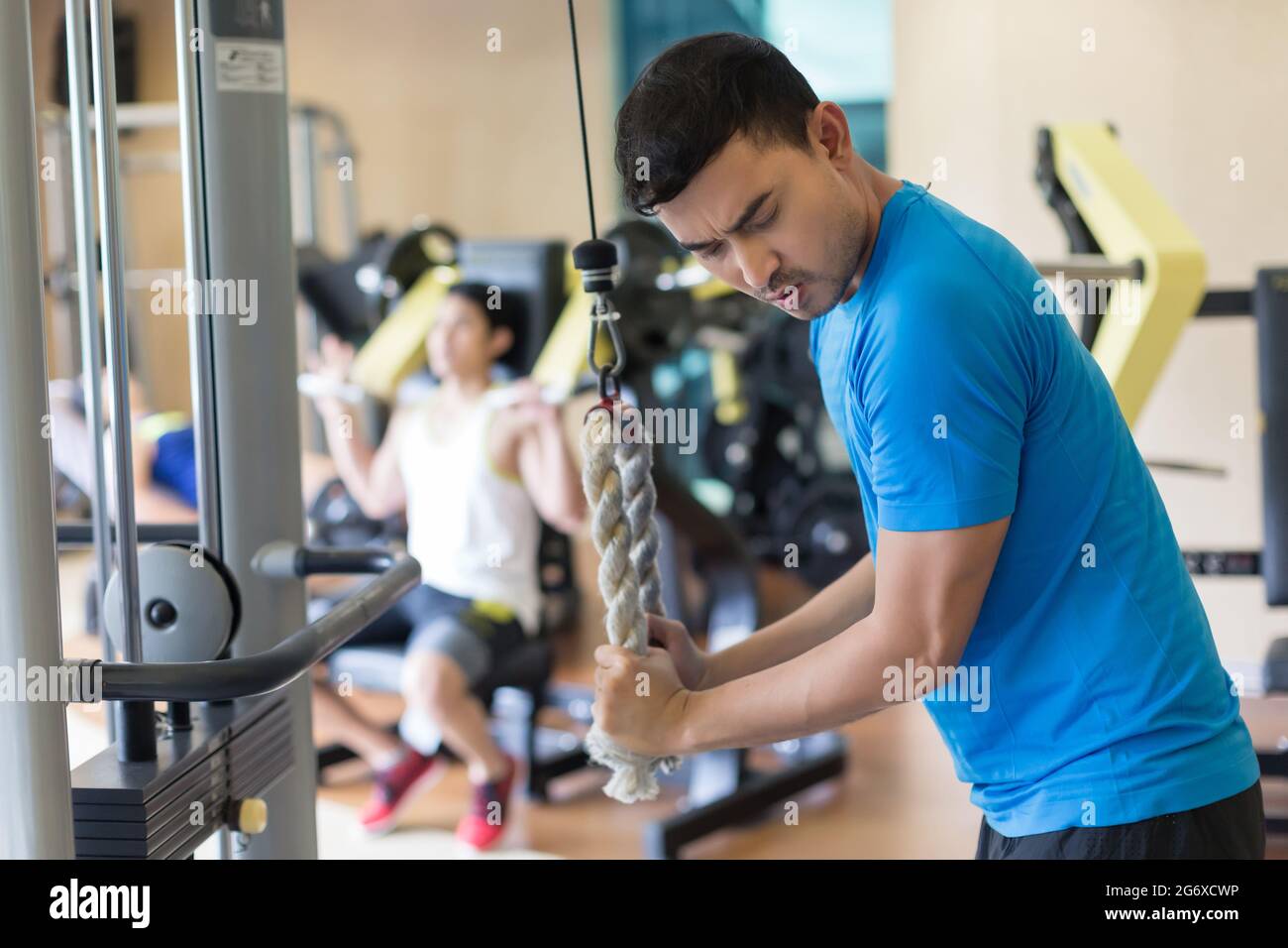 Seitenansicht eines jungen Mannes, der beim Training von Trizeps am Seilzuggerät während des intensiven Trainings im Fitnessstudio ausatmet Stockfoto