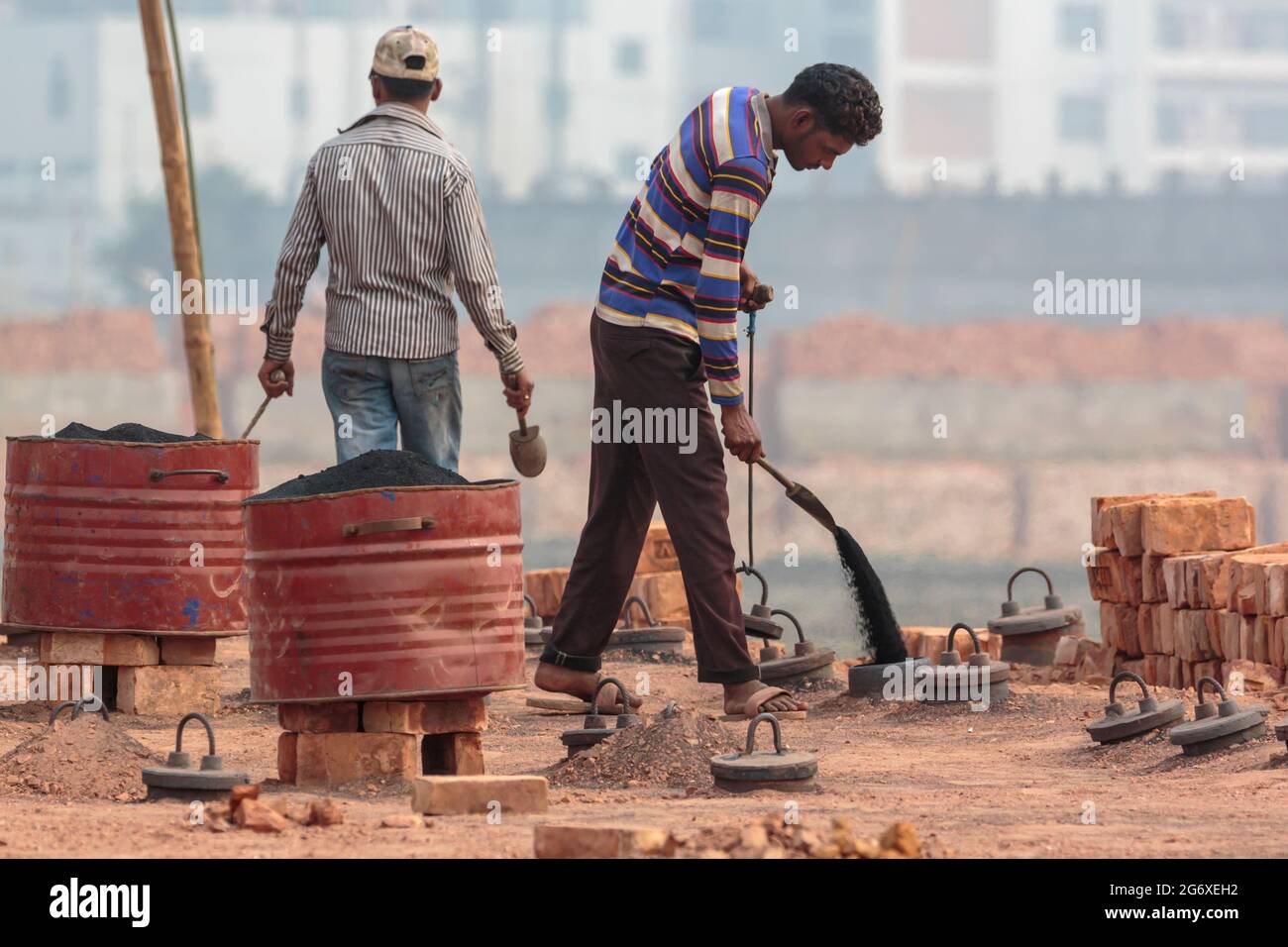 Arbeiter, die Kohlenstaub in den Ziegelofen i Ashulia außerhalb von Dhaka gießen. Es gibt modernere und weniger umweltschädliche Methoden zur Herstellung von Ziegelsteinen, aber in Bangladesch treiben die Arbeitskosten und die Rohstoffkosten die hochgradig unregulierte Ziegelindustrie an. Aufgrund der hohen Nachfrage nach billigen Baumaterialien hat sich die Ziegelherstellung aus Lehm in Bangladesch zu einer florierenden Industrie entwickelt, wobei die Herstellung von Öfen stark in den Rängen größerer Städte und Städte konzentriert ist. Diese Produktionsstandorte, bekannt als brickfields, arbeiten mit jahrhundertealten Technologien, die Staub, Asche, schwarzen Rauch und andere Schadstoffe vertreiben Stockfoto