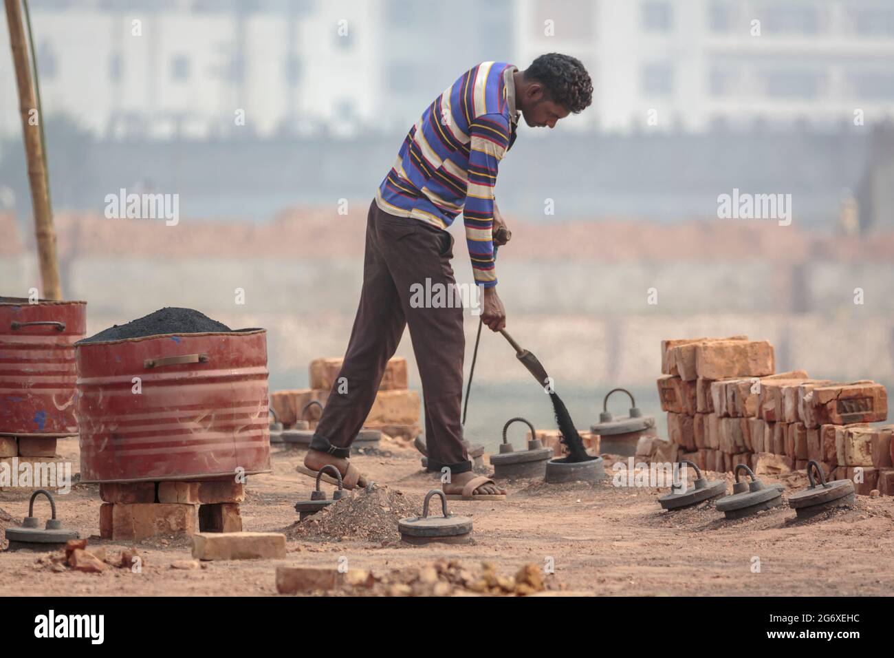 Arbeiter, die Kohlenstaub in den Ziegelofen i Ashulia außerhalb von Dhaka gießen. Es gibt modernere und weniger umweltschädliche Methoden zur Herstellung von Ziegelsteinen, aber in Bangladesch treiben die Arbeitskosten und die Rohstoffkosten die hochgradig unregulierte Ziegelindustrie an. Aufgrund der hohen Nachfrage nach billigen Baumaterialien hat sich die Ziegelherstellung aus Lehm in Bangladesch zu einer florierenden Industrie entwickelt, wobei die Herstellung von Öfen stark in den Rängen größerer Städte und Städte konzentriert ist. Diese Produktionsstandorte, bekannt als brickfields, arbeiten mit jahrhundertealten Technologien, die Staub, Asche, schwarzen Rauch und andere Schadstoffe vertreiben Stockfoto