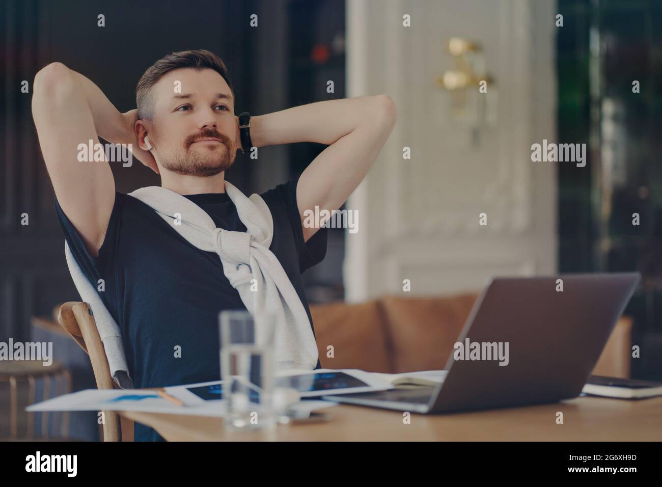 Nachdenklicher bärtiger Mann denkt über die Aufgabe nach hält die Hände hinter dem Kopf sitzt auf dem Schreibtisch mit modernen Gadgets denkt über die Distanz Job konzentriert sich in der Ferne Stockfoto