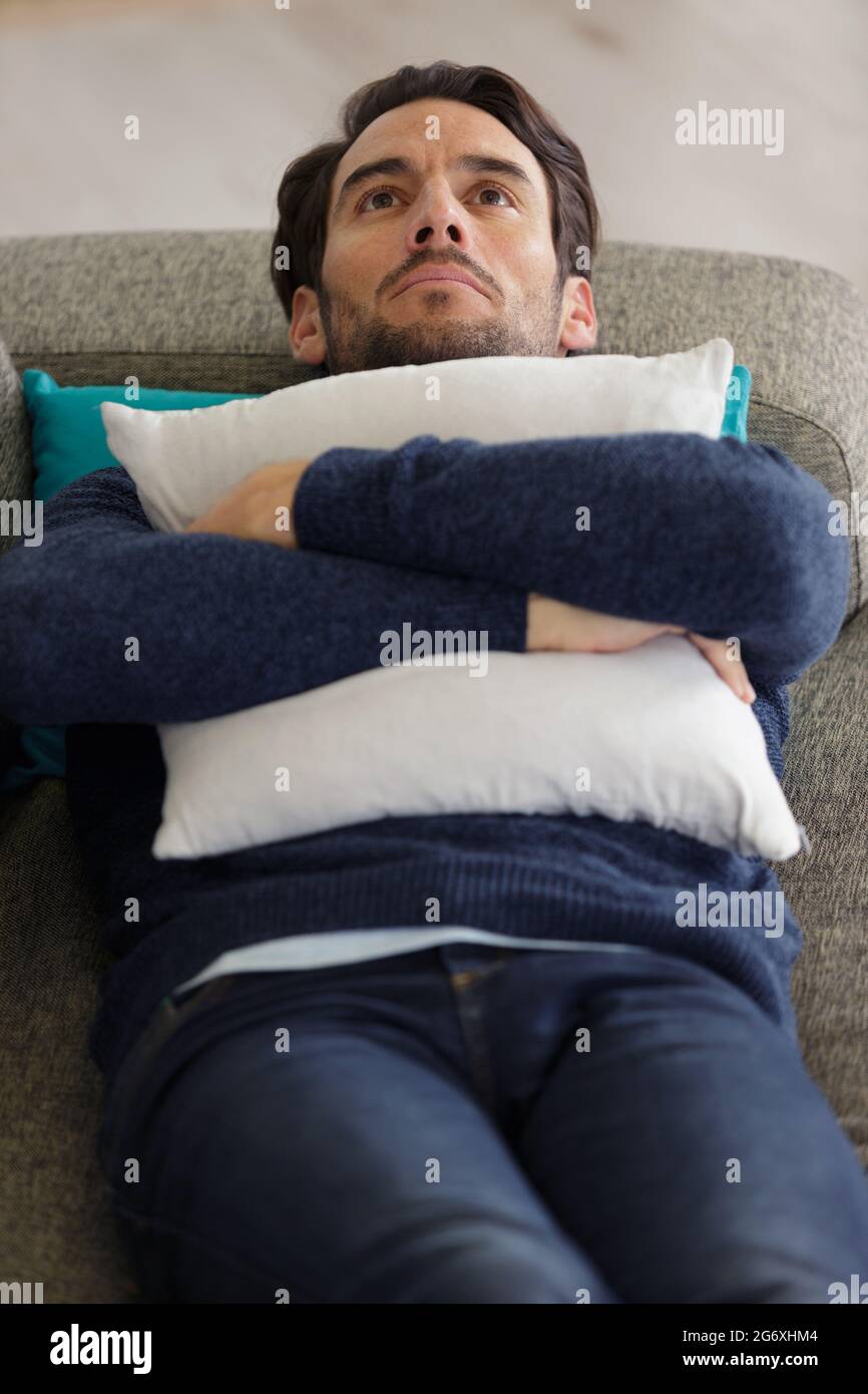 Nachdenklicher Mann umarmte Kissen auf dem Sofa Stockfoto