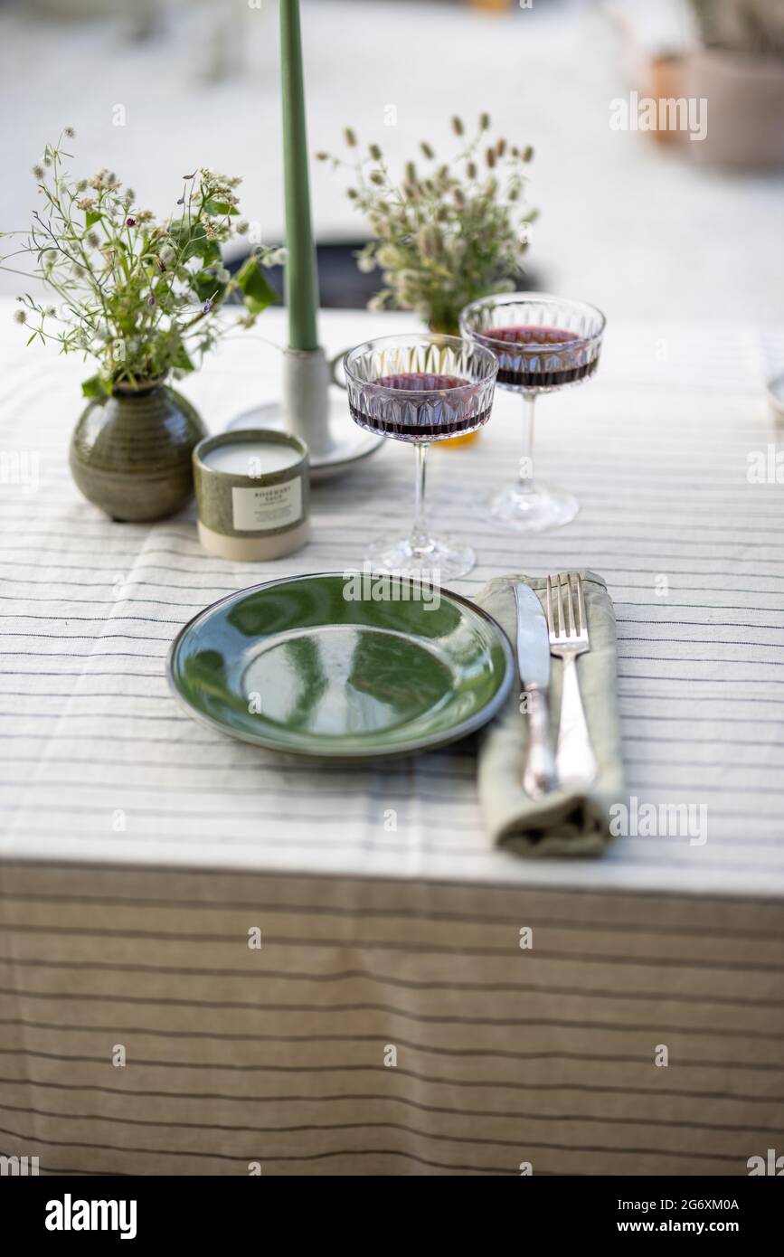 Der Tisch im Garten ist mit einer Tischdecke bedeckt und mit Blumen und Kerzen mit Essen für zwei Personen geschmückt. Abendessen im Sommer im Freien. Grüner und natürlicher Stil. Stockfoto
