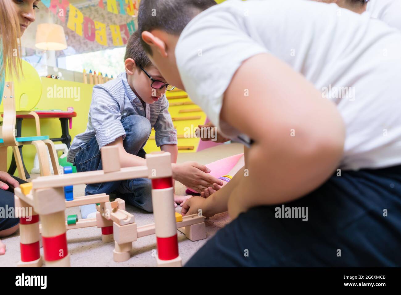 Cute boy Brillen tragen, während sie mit Aufmerksamkeit und Geduld eine hölzerne Struktur während einer pädagogischen Gruppe Aktivität im Kindergarten Stockfoto