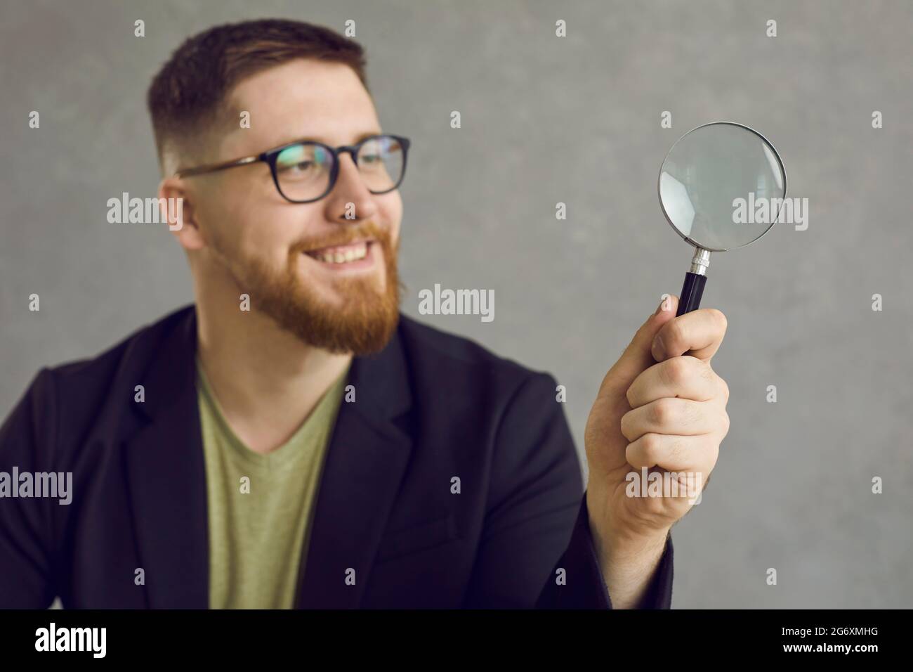 Fröhlicher junger Student oder Geschäftsmann in einer Brille, der durch eine Lupe schaut Stockfoto