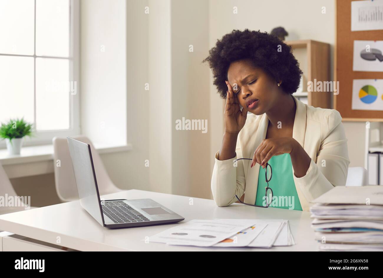 Müde junge Frau mit dunkler Haut, die starke Kopfschmerzen hat und bei der Arbeit vor dem Laptop sitzt. Stockfoto