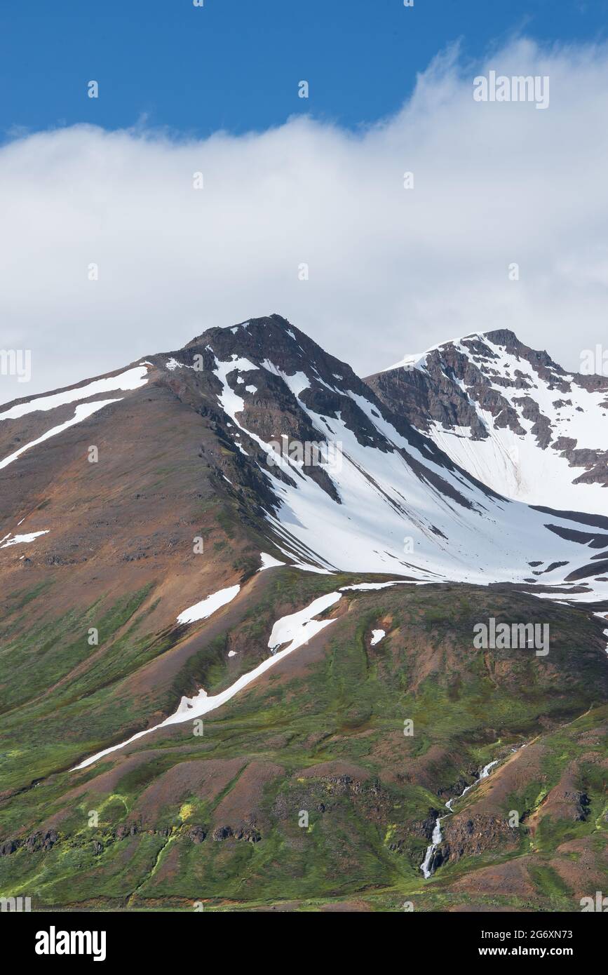Schneebedeckter Berg mit weißen geschwollenen Wolken und einem klaren blauen Himmel in Island im Sommer. Stockfoto