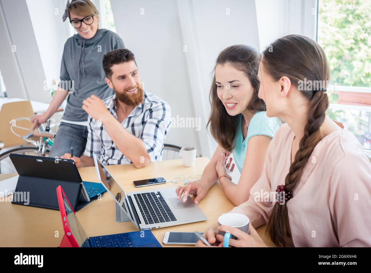 Junge, kompetente Mitarbeiter, die lächeln und zusammenarbeiten, nutzen mobile drahtlose Technologie für Telearbeit in einem modernen, gemeinsam genutzten Bürobereich Stockfoto