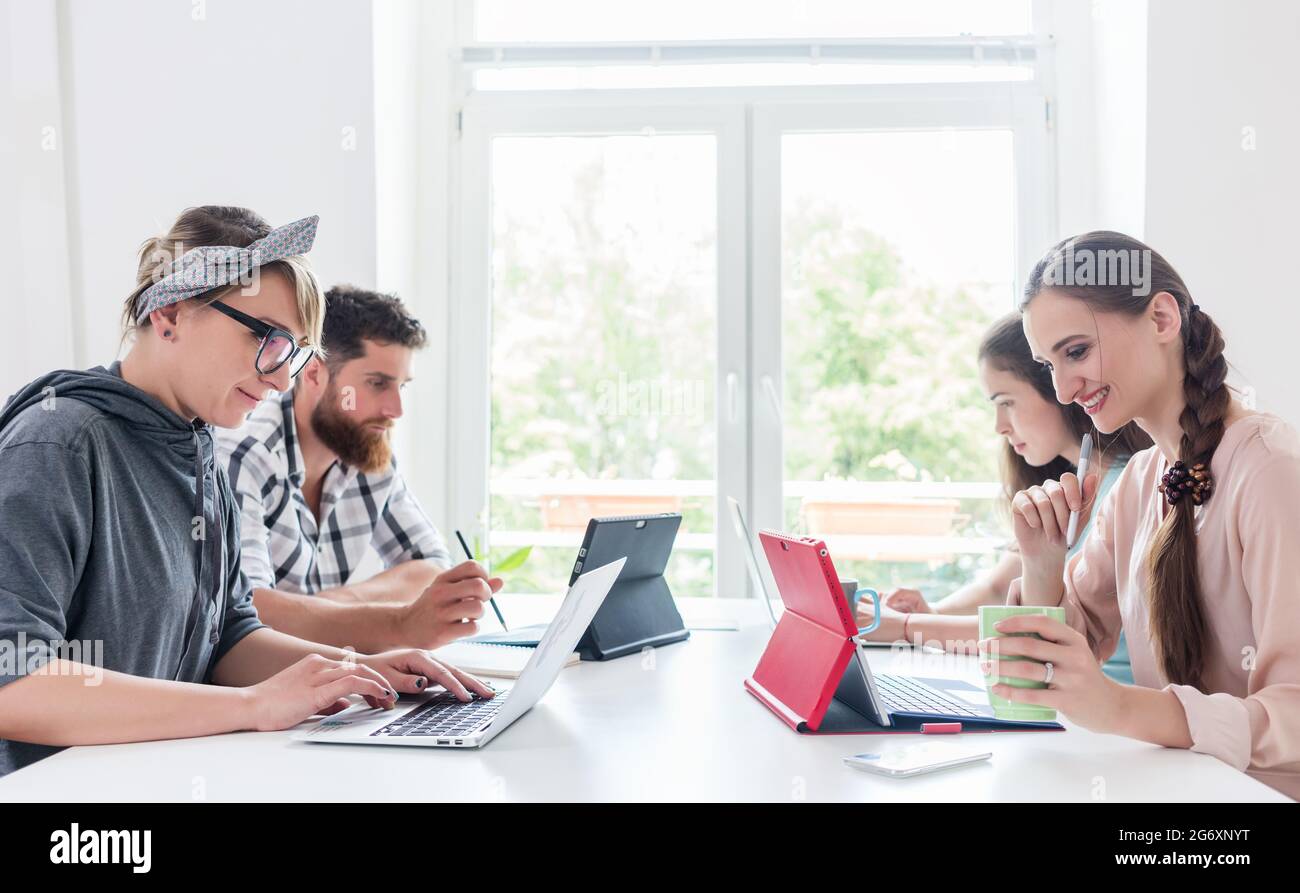 Seitenansicht von vier engagierten jungen Menschen, die sich einen Schreibtisch teilen, während sie in einem modernen Co-Working-Space für Freiberufler und unabhängige Auftragnehmer arbeiten Stockfoto