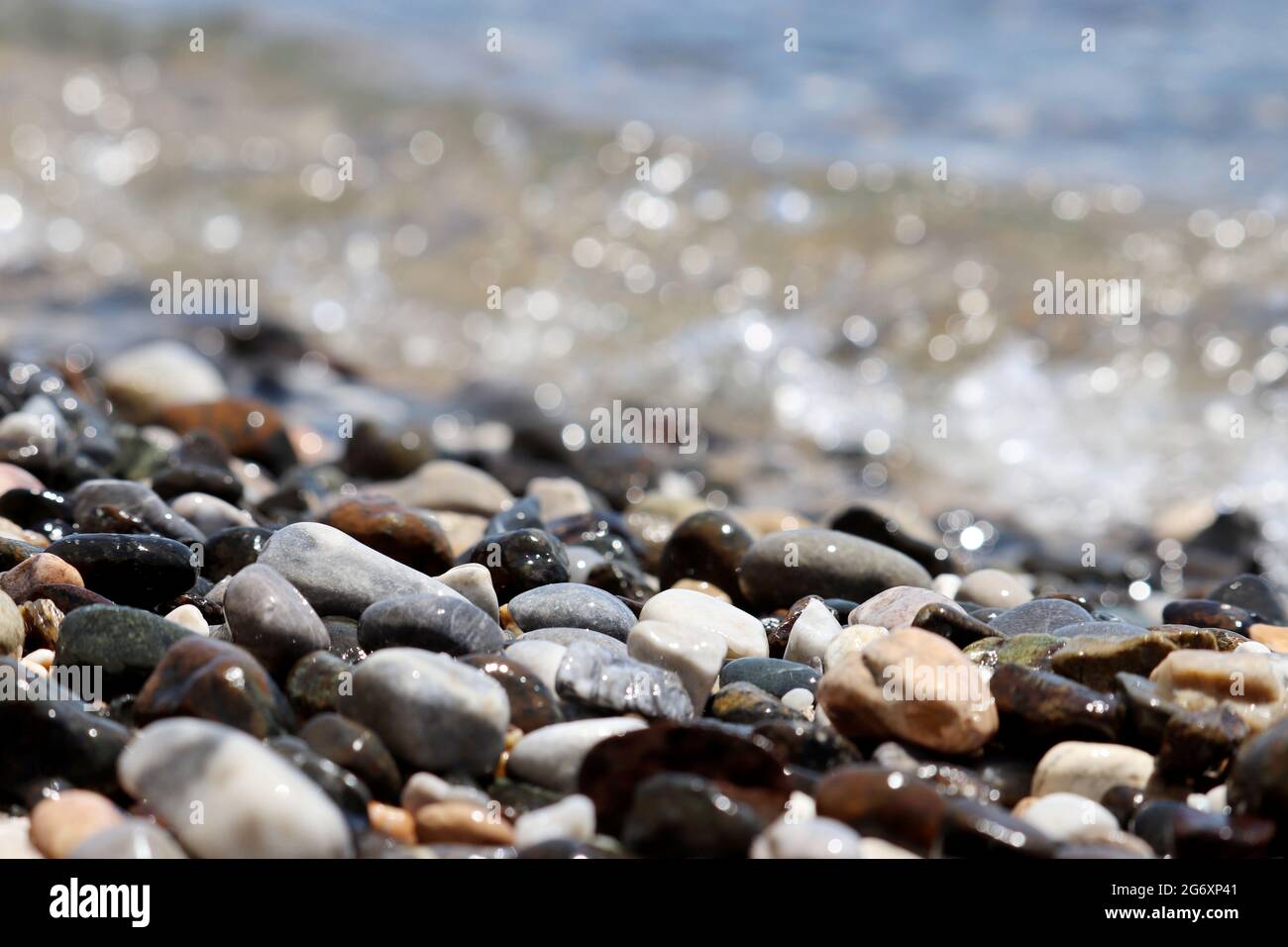 Nasse Kieselsteine auf unscharfem Hintergrund von Meereswellen. Strandurlaub im Sommer Stockfoto