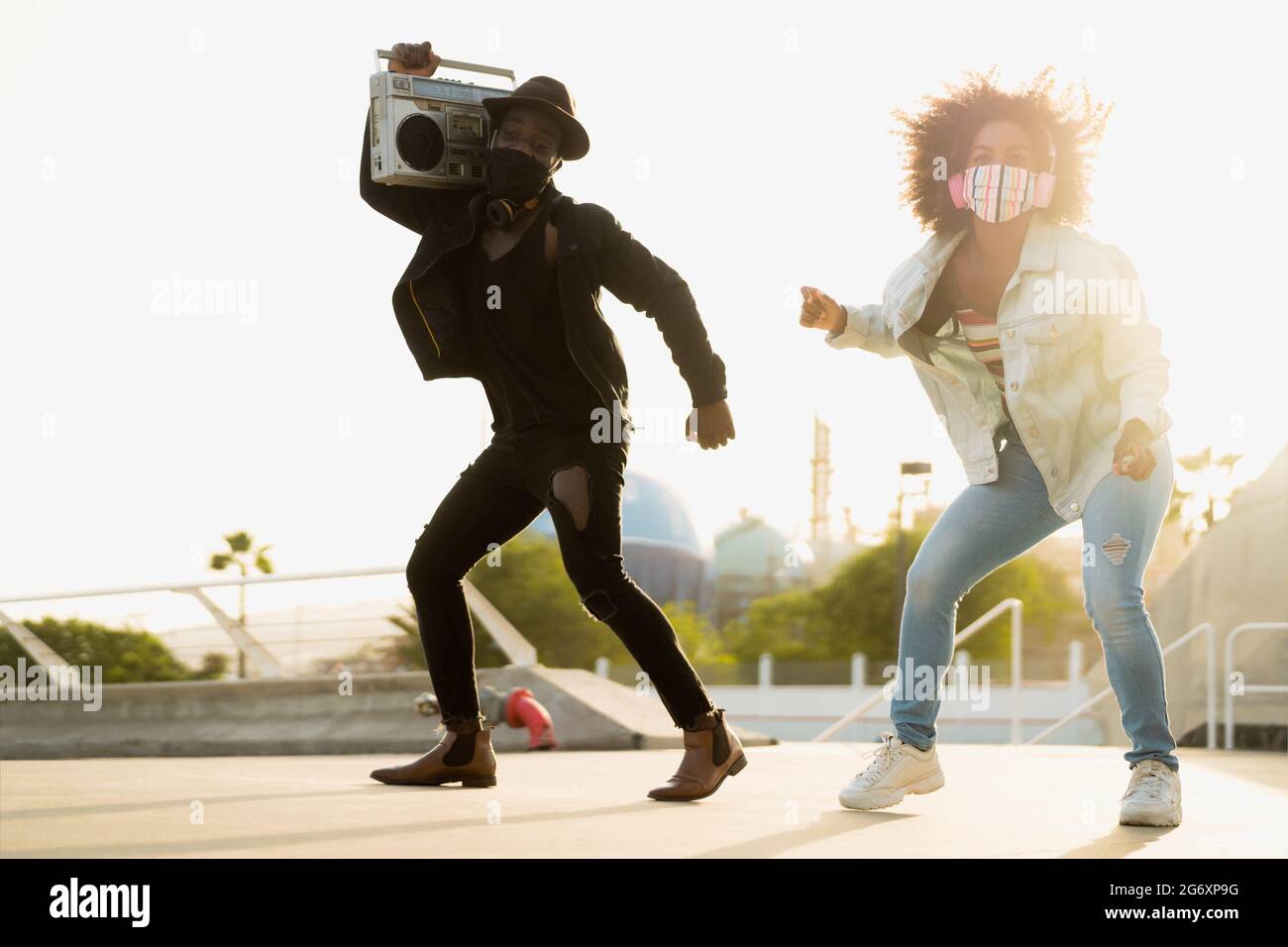 Junge Afro-Freunde tanzen draußen, während sie Musik mit hören Kabellose Kopfhörer und Vintage-Boombox Stockfoto