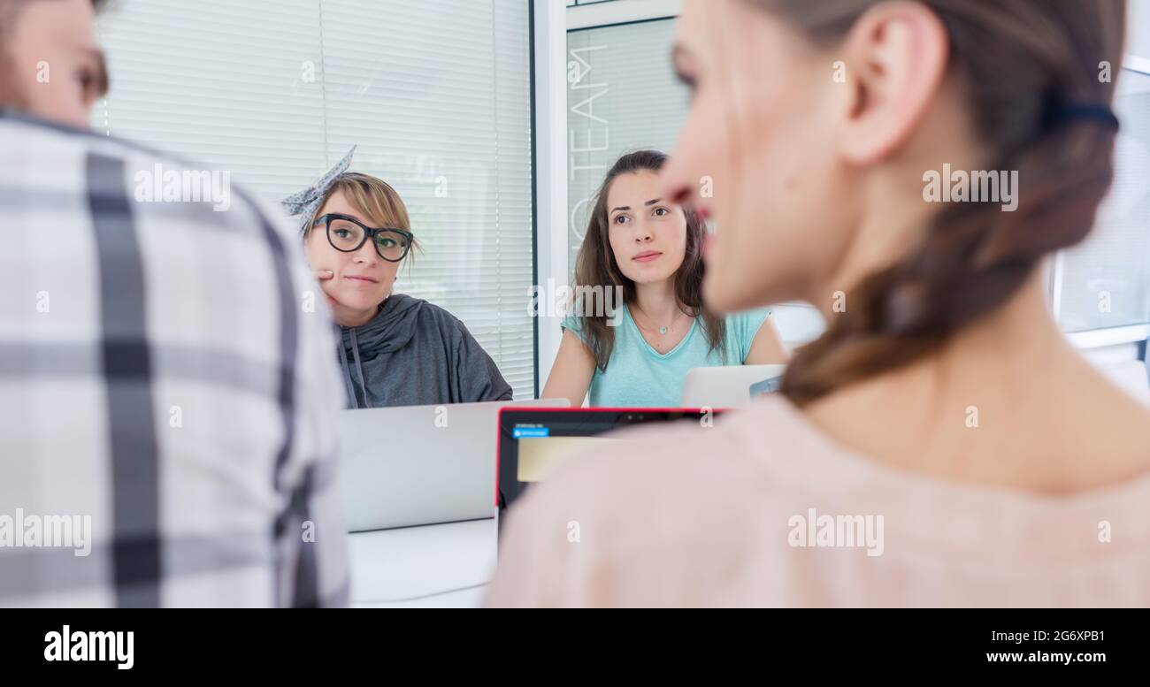 Seitenansicht eines kreativen weiblichen Freiberufler lächelnd zu ihr Mitarbeiter, während Sie einen Anruf auf dem Mobiltelefon in einem gemeinsamen Schreibtisch in entspannter Arbeiten environ Stockfoto